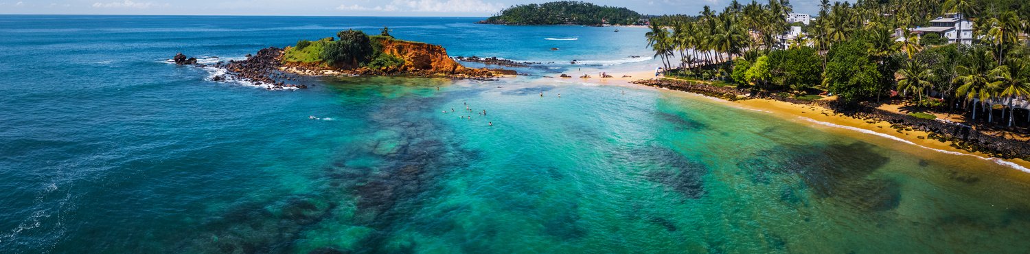 Aerial panorama of the tropical beach and clear sea with coral reefs in the town of Mirissa, Sri Lanka